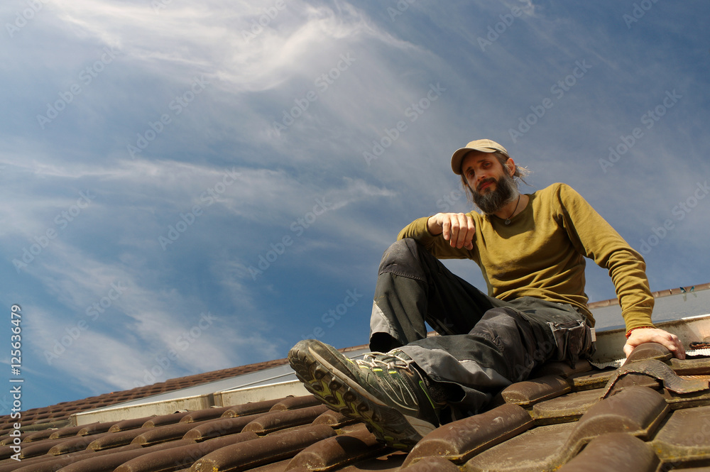 bearded roofer resting on top of a roof sunny day bearded roofer resting on top of a roof sunny day