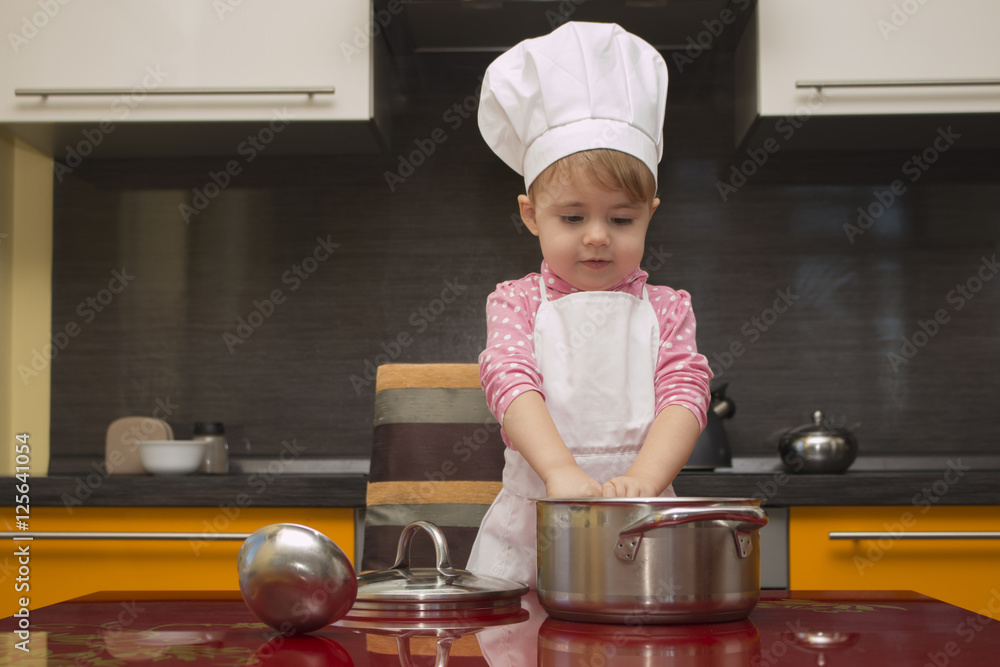The small child in chef suit helps her mother cook in the kitchen The small child in chef suit helps her mother cook in the kitchen