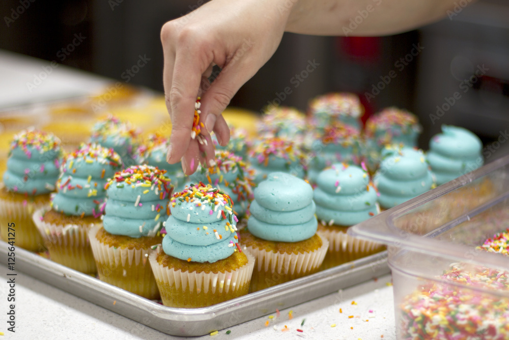 Baker Decorating Vanilla Cupcakes with Blue Frosting