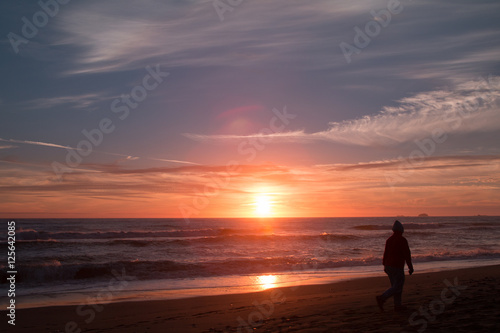 A woman walks on the beach at sunset.