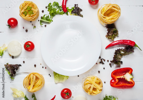 Ingredients for cooking spagetti, cherry tomatoes, pepper around a white plate place text, frame on wooden rustic background top view