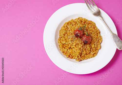 A dinner bowl of tomato risotto on a bright pink background