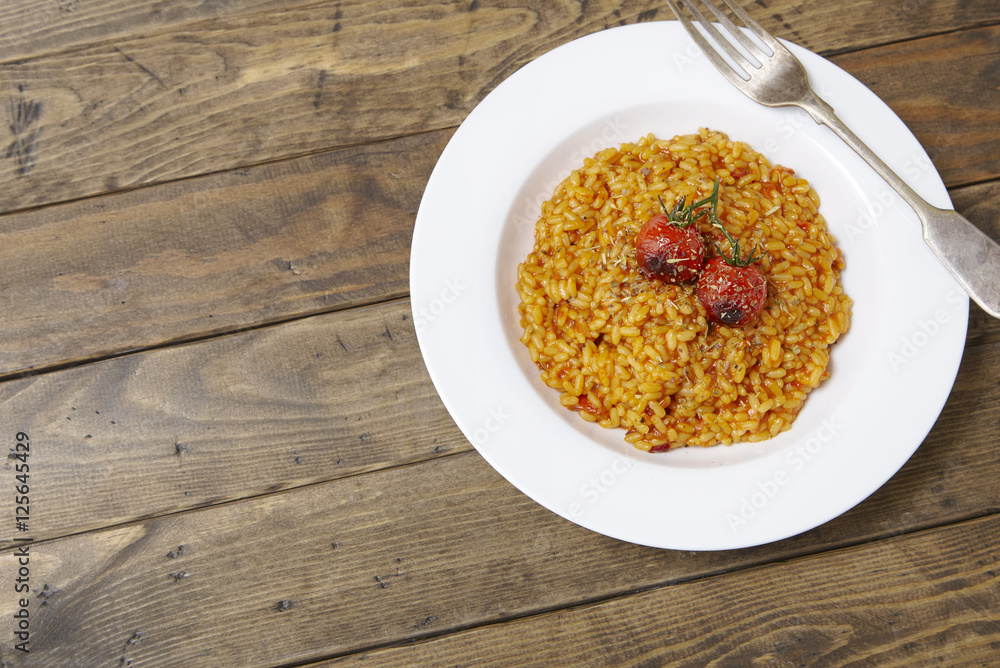 A dish of tomato risotto on a rustic wooden dinner table background forming a page border A dish of tomato risotto on a rustic wooden dinner table background forming a page border