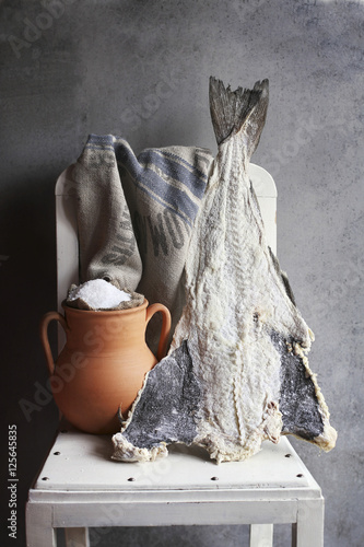 Salted cod fish and rustic pot with sea salt on white chair photo