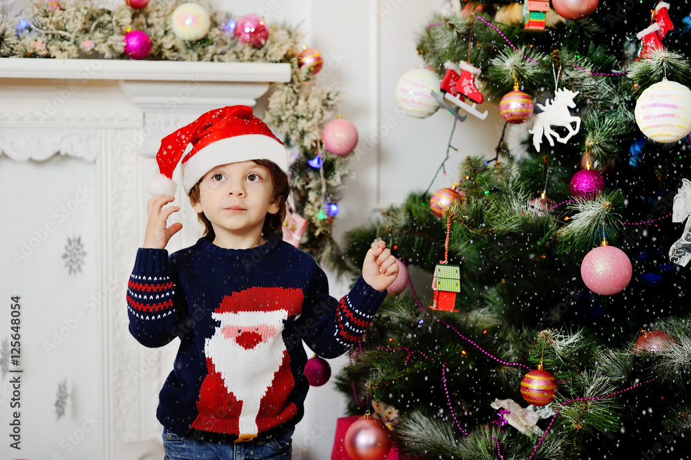 treecute baby wearing a sweater with Santa Claus on a background of the Christmas tree