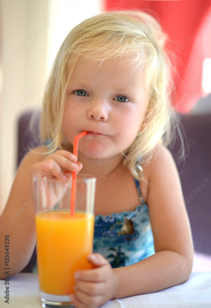 Little baby girl drink orange juice from highball glass with str Stock Adobe Stock