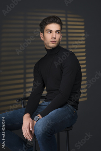 Stylish young man in a black sweater sits near blinds and thinki © rozaivn58