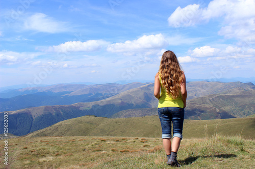 The girl tourist with long hair looks at the mountains in clear