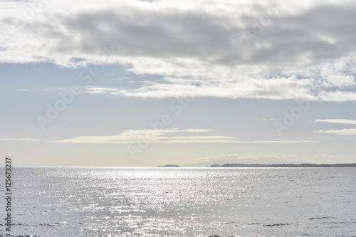 Silver ocean with cloudy sky above and flat landmass in distance.