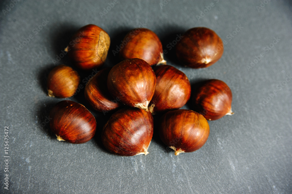 Fototapeta premium raw edible chestnuts close up on slate background. top view