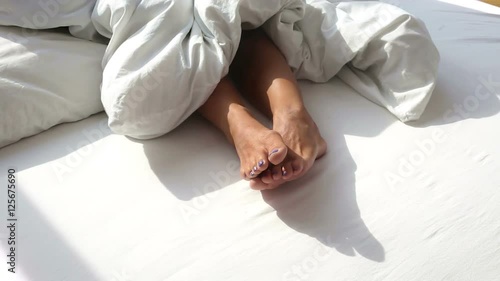 closeup of bare feet of woman in bed on a sunny morning with the blanket being pulled
