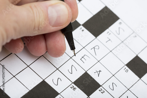 A person is doing a crossword puzzle. The word stress is written on it. Good training for brains for elderly people and stress relieve. Focus point on the pen tip.