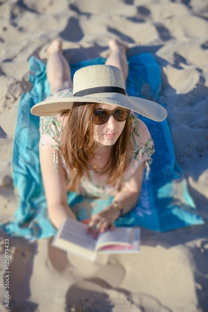 Portrait of a young brunette relaxing on the beach, reading a bo