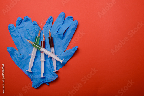 Hand in glove with syringe on red background.