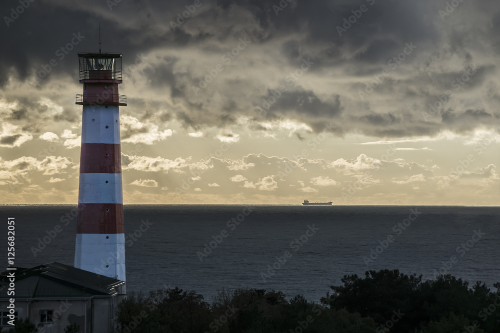 Lighthouse on the sea under stormy clouds and with the ship in the background