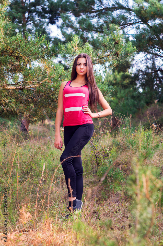 Young beautiful brunette model posing in the sports image of the park against the backdrop trees Young beautiful brunette model posing in the sports image of the park against the backdrop trees