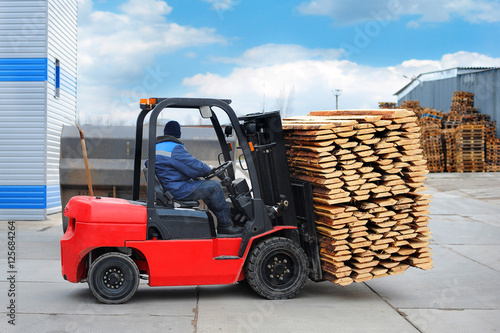 Red forklift transports the boards at the plant for woodworking.