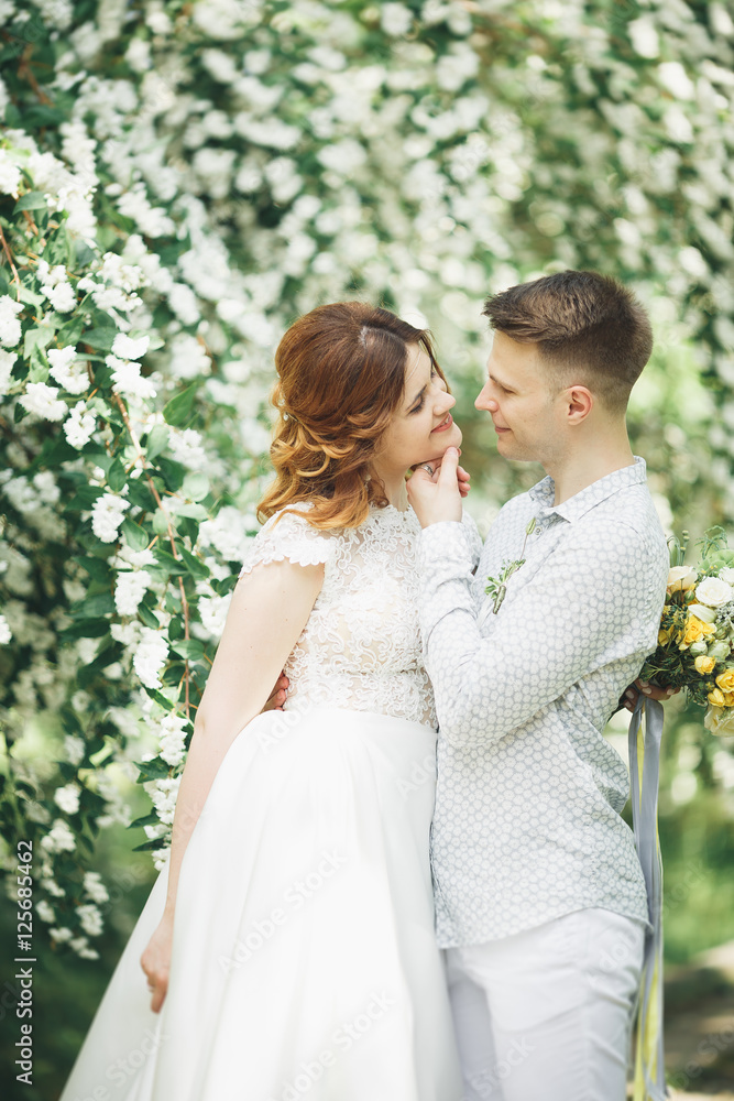 Stylish couple of happy newlyweds walking in the park on their wedding day with bouquet Stylish couple of happy newlyweds walking in the park on their wedding day with bouquet