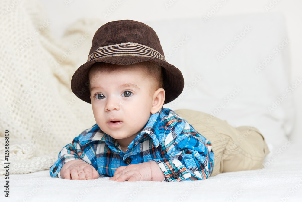 baby portrait lie on white towel in bed, dressed in plaid shirt and hat baby portrait lie on white towel in bed, dressed in plaid shirt and hat