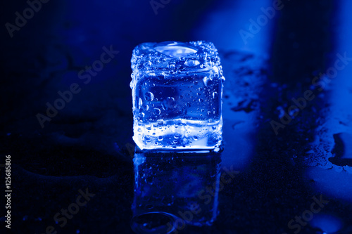 Pile of different wet ice cubes on black background with blue li © peterkai