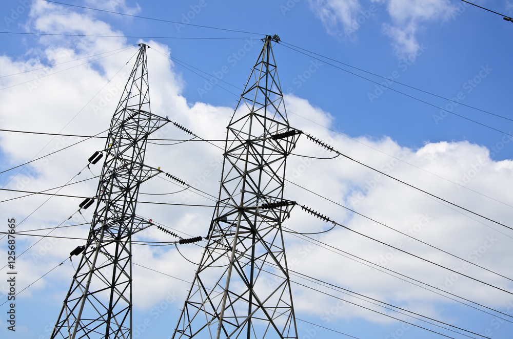 High voltage power lines with electricity pylons at blue sky.