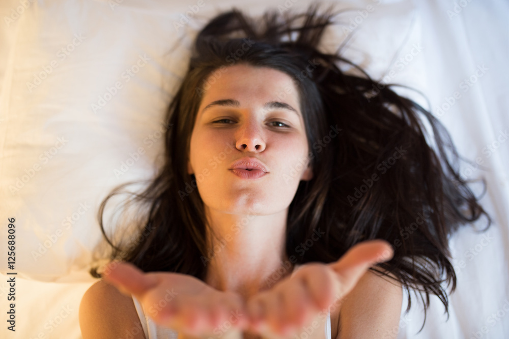 Brunette attractive and beautiful young woman on the white bed in white t-shirt, playing and give air kiss. Brunette attractive and beautiful young woman on the white bed in white t-shirt, playing and give air kiss.