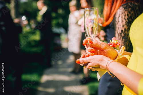 A woman in yellow dress is holding a glass with a beverage champagne outside at a party. Copy space. Place for the text. Outdoor catering social. People outdoor. Copy space.