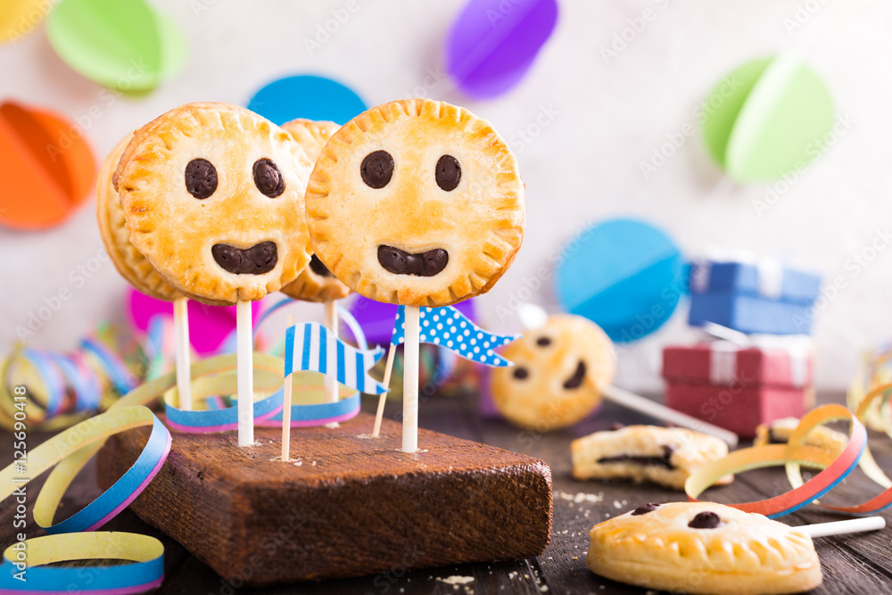 Homemade shortbread smiley cookies with dark chocolate on stick called pie pops. Children's party background.