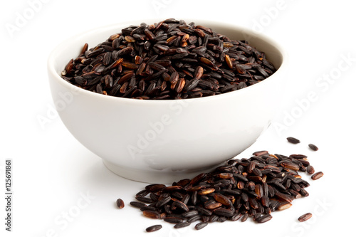 Bowl of Nerone black long grain rice isolated on white. Spilled rice.
