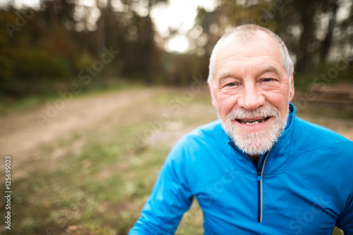 Senior runner in nature. Man resting, smiling. Close up.