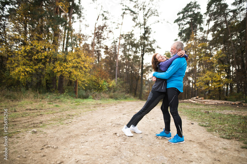 Beautiful senior couple running outside in sunny autumn forest