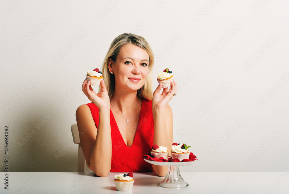 Beautiful young blond woman sitting at the table, holding home made cupcakes Beautiful young blond woman sitting at the table, holding home made cupcakes