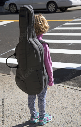 New York USA - October 2016 - Little girl carrying a cello in a case waits at the kerb to cross a road