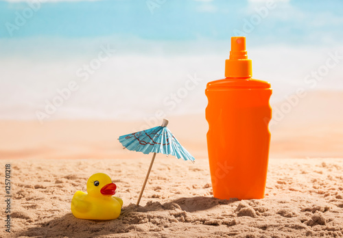 Fotografie Sunscreen, umbrella and rubber duck in sand against sea.