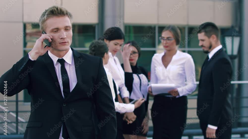 Portrait of smart-city business man talking on the phone and business people in background discussing the cooperative plans Portrait of smart-city business man talking on the phone and business people in background discussing the cooperative plans