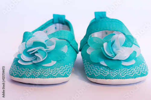 Two isolated turquoise green baby girl shoes with a flower on the toe on white background 