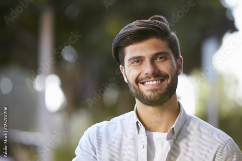 Smiling bearded young man sitting outside, portrait
