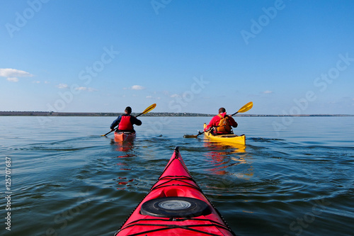 Two guys in a kayak. Kayaking in the calm blue lake. View from the red kayak.