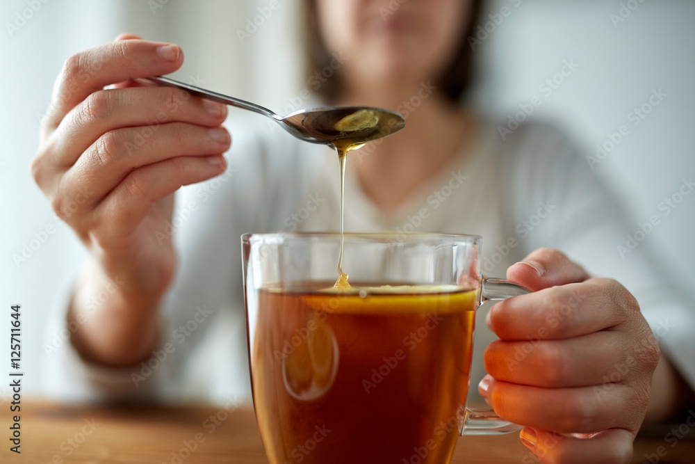 close up of woman adding honey to tea with lemon close up of woman adding honey to tea with lemon
