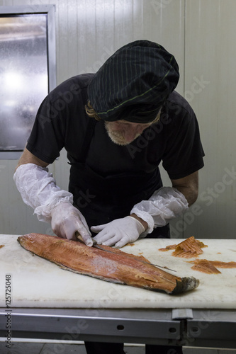 Fish smoker cleaning freshly smoked salmon with a knife