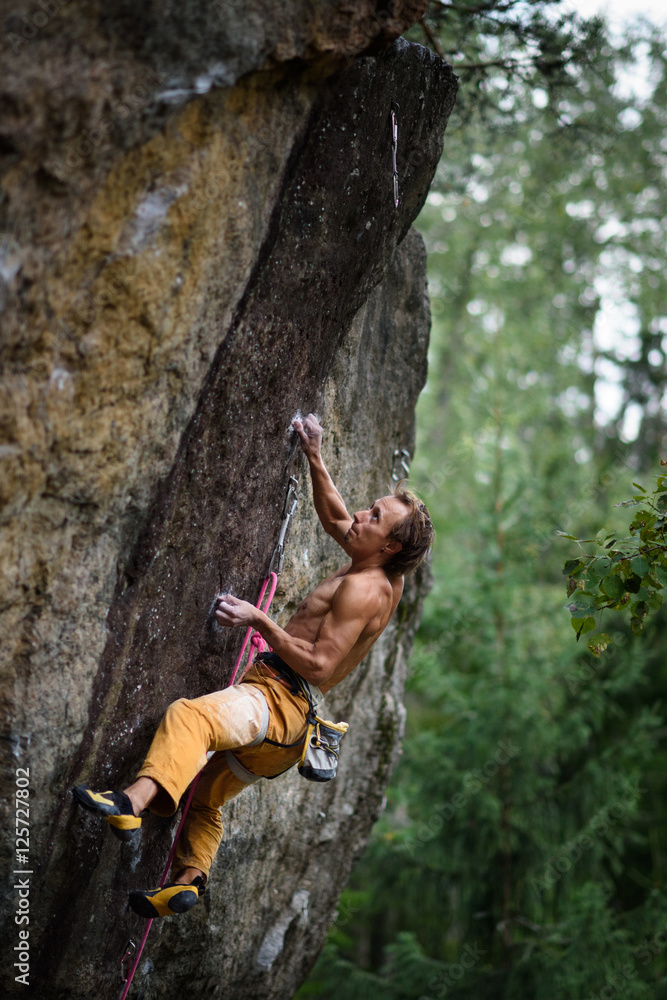 Fototapeta premium Extreme sport climbing. Young male rock climber on a rock wall.