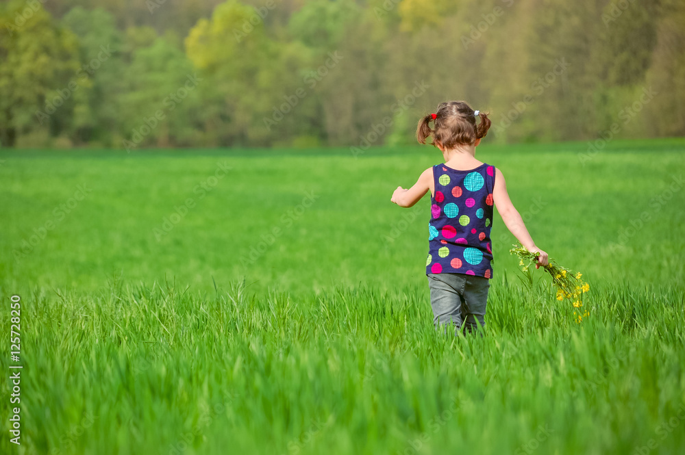 Fototapeta premium Child with flowers bouquet on green spring field, kid having fun outdoors 