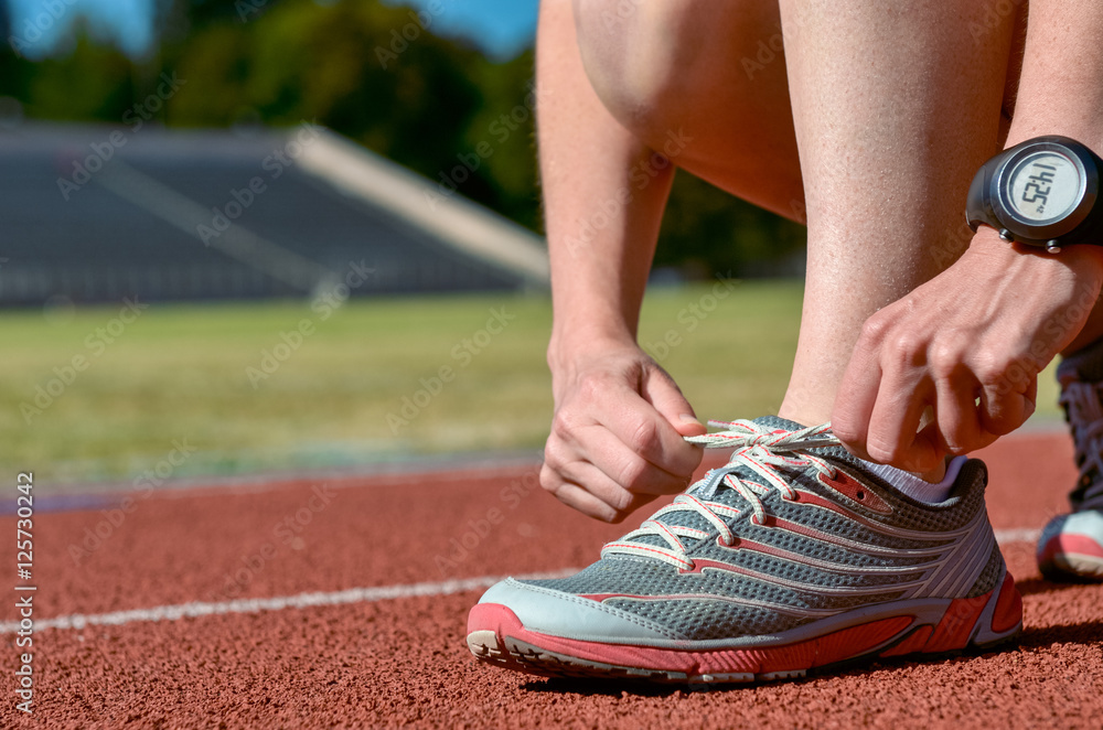 Running shoes closeup, female runner athlete tying laces for training and jogging on stadium track, sport and fitness concept
