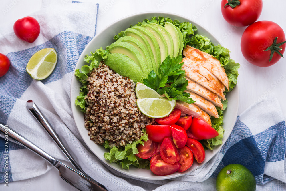 Plakat Healthy salad bowl with quinoa, tomatoes, chicken, avocado, lime and mixed greens (lettuce, parsley) on white wood background top view. Food and health. Superfoods meal.