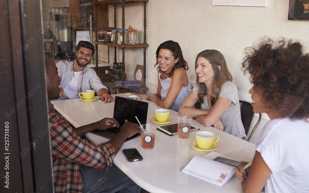 Obraz premium Young adult friends hanging out in cafe, seen through window