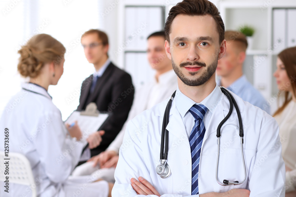 Friendly male doctor on the background doctor and many patients Friendly male doctor on the background doctor and many patients