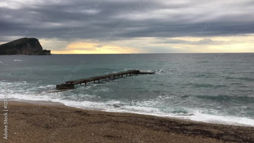 Mediterranean beach in sunset with waves bashing in a pier and an island in background Mediterranean beach in sunset with waves bashing in a pier and an island in background