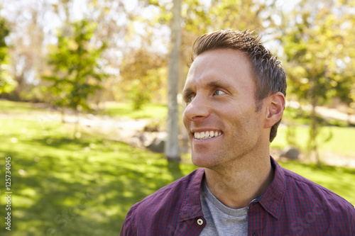 Happy adult man in park looking away from camera, close up