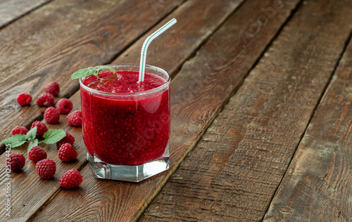 Raspberry smoothie in glass with straw on wood table