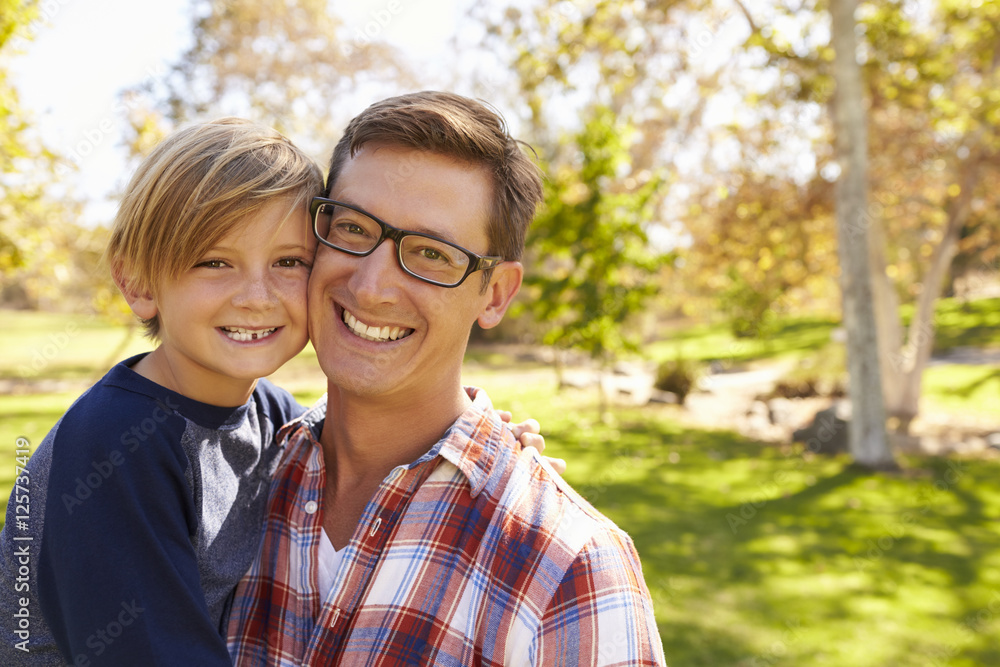 Father and seven year old son smiling to camera in a park Father and seven year old son smiling to camera in a park